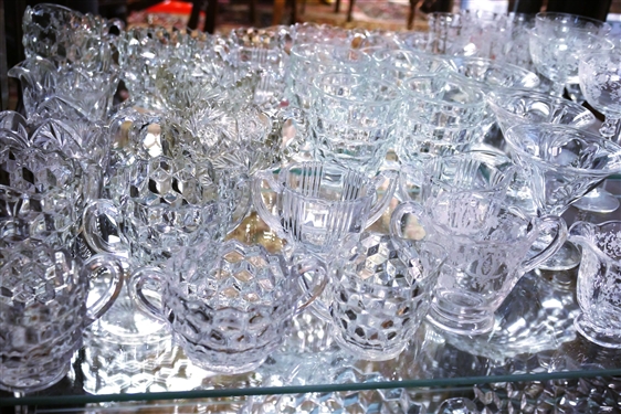 2 Shelves of Clear Glassware including American Fostoria Champagnes, American Fostoria Iced Teas, American Fostoria Cream & Sugars, Elegant Etched Glass Pieces, and Press Glass Cream and Sugar
