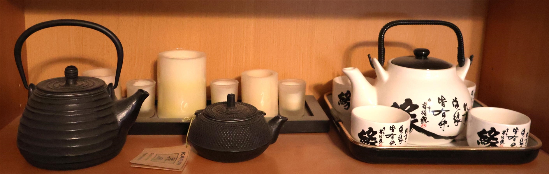 Shelf Lot including Kafuh Cast Iron Tea Kettle, Larger Cast Iron Tea Kettle, Tray of Candles, and Asian Tea Set with Tray and Cups