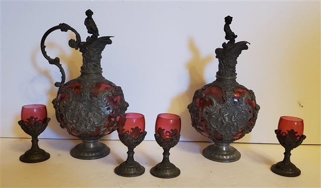 Outstanding Cranberry Glass Decanter and Cordial Set - Framed with Scrollwork and Cherubs - 1 Decanter with Handle and 1 Without - Decanter Measures 9 Tall 