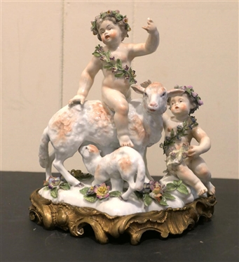 German Porcelain Lamb and Putti Figure - Delicate Porcelain Flowers on Base, and Crowns -Ornate Metal Base - Figure is 8" Tall 8" Across - Few Small Broken Petals, Fingers on Putti are Broken 