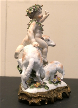 German Porcelain Lamb and Putti Figure - Delicate Porcelain Flowers on Base, and Crowns -Ornate Metal Base - Figure is 8 Tall 8 Across - Few Small Broken Petals, Fingers on Putti are Broken 