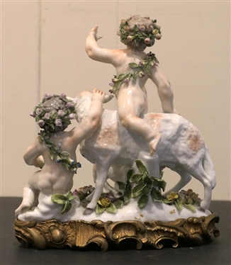 German Porcelain Lamb and Putti Figure - Delicate Porcelain Flowers on Base, and Crowns -Ornate Metal Base - Figure is 8 Tall 8 Across - Few Small Broken Petals, Fingers on Putti are Broken 