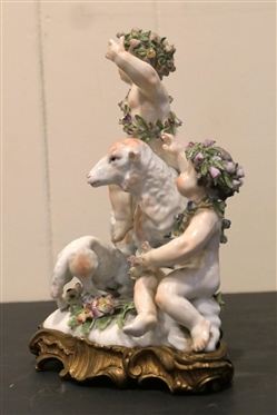German Porcelain Lamb and Putti Figure - Delicate Porcelain Flowers on Base, and Crowns -Ornate Metal Base - Figure is 8 Tall 8 Across - Few Small Broken Petals, Fingers on Putti are Broken 